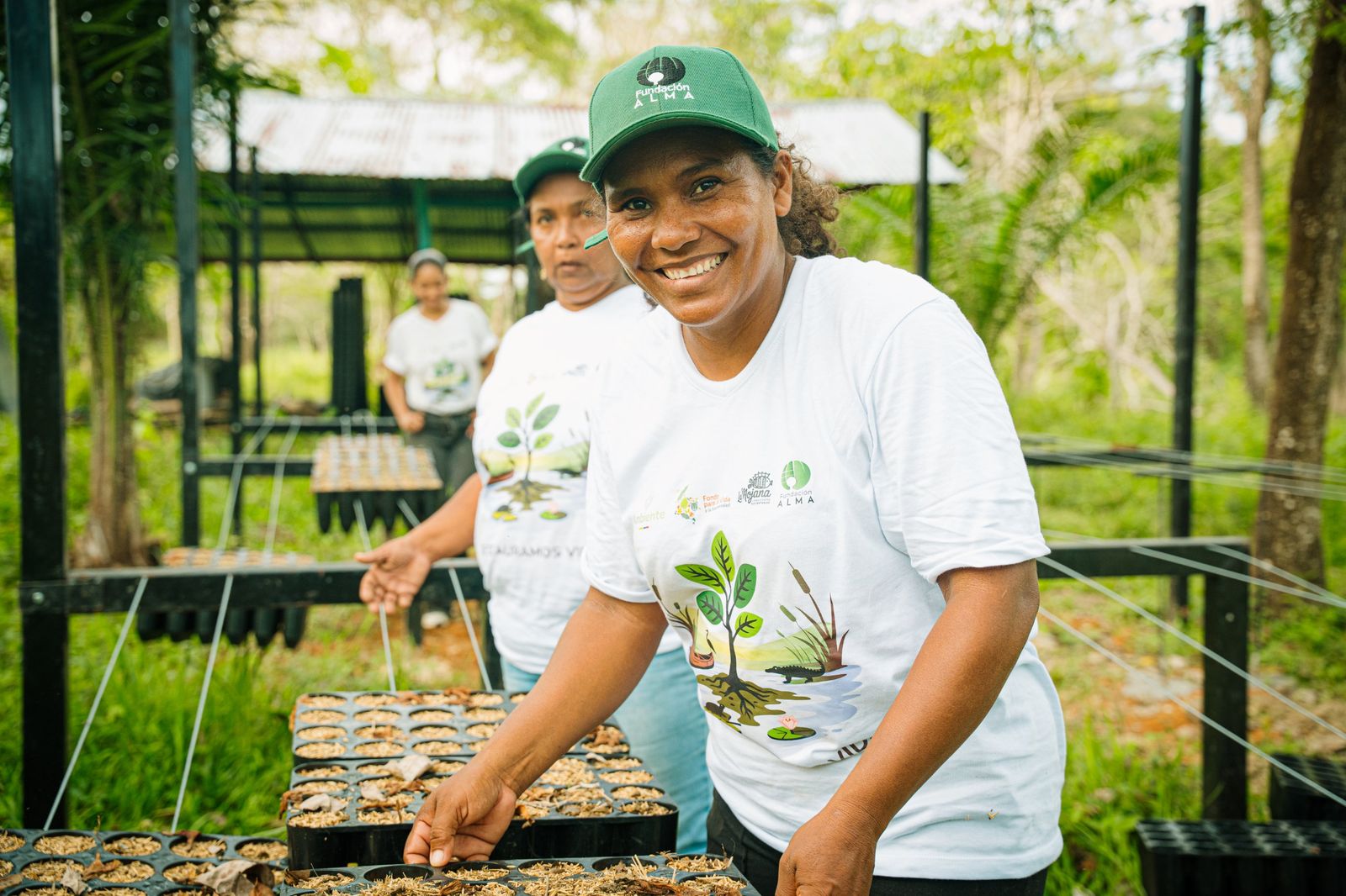 Mujer sonriendo con la gorra de Fundación ALMA mientras trabaja en un vivero de especies nativas